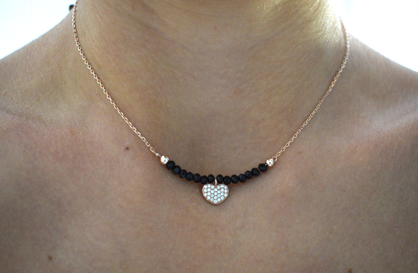 Collana indossata composta da un cuoricino rosé con zirconi al centro e 7 perline nere al lato del ciondolo con catenina rosè