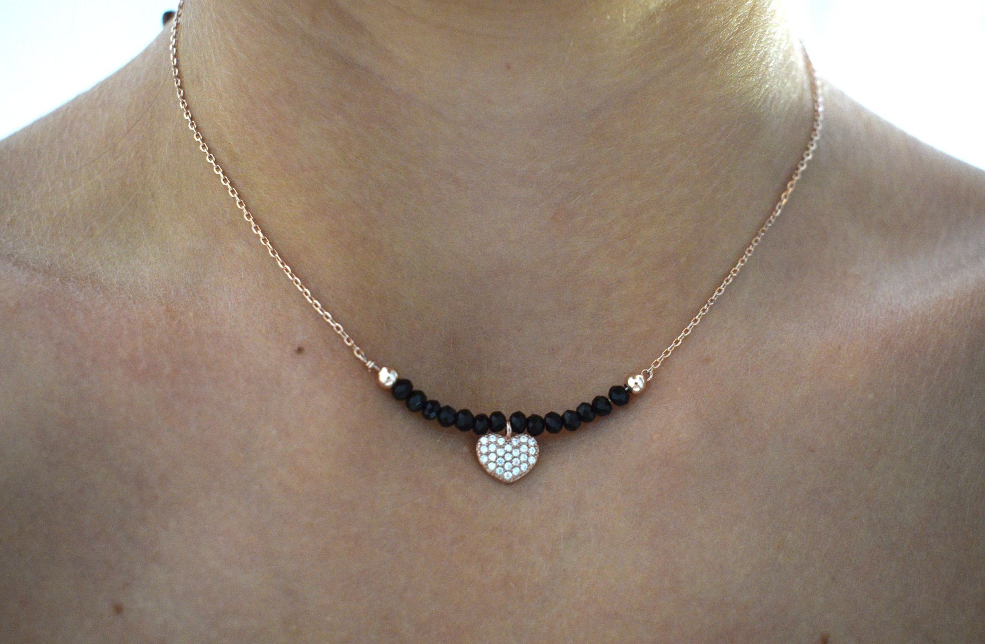 Collana indossata composta da un cuoricino rosé con zirconi al centro e 7 perline nere al lato del ciondolo con catenina rosè